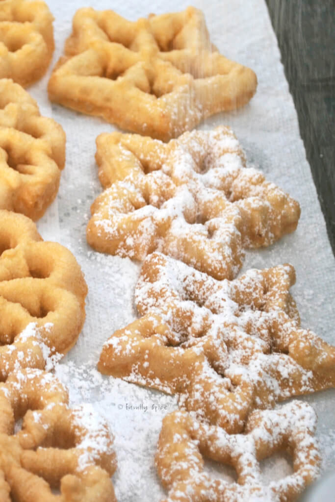 Various rosettes freshly fried being dusted with powdered sugar