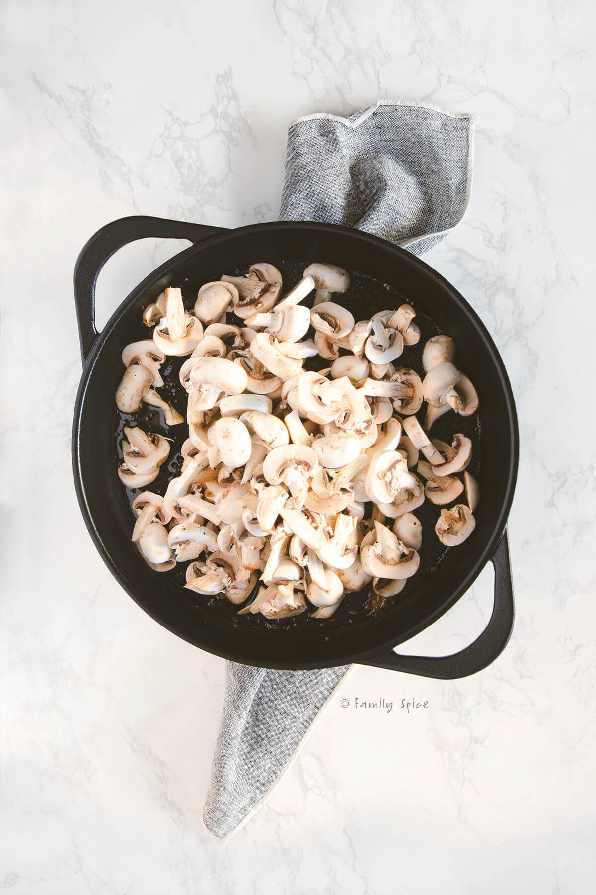 Adding sliced mushrooms to a large cast iron pan