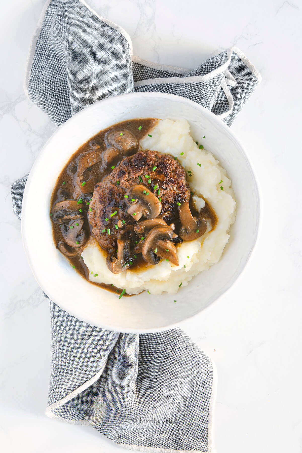 Closeup of a shallow bowl with mashed potatoes and salisbury steak with mushroom gravy