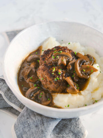 Side view of a shallow bowl with mashed potatoes and salisbury steak with mushroom gravy