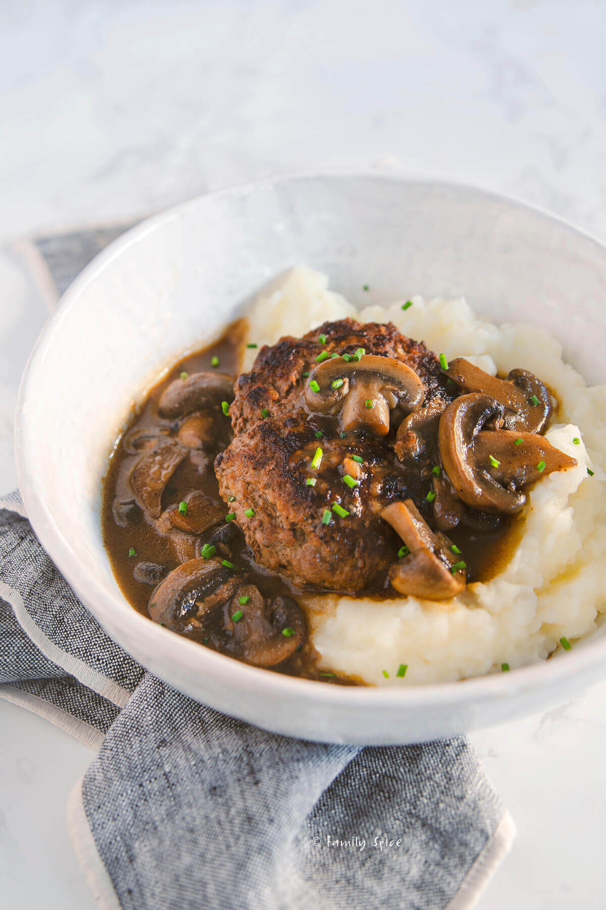 Side view of a shallow bowl with mashed potatoes and salisbury steak with mushroom gravy