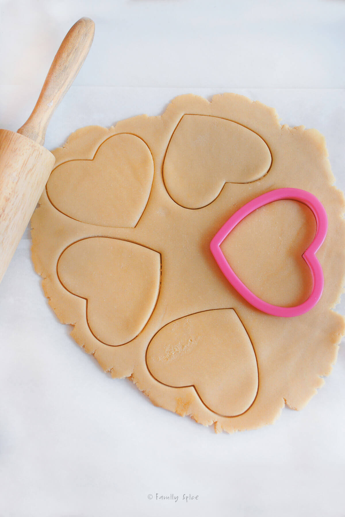 Sugar cookie dough rolled flat with heart cookie cutter cutting it