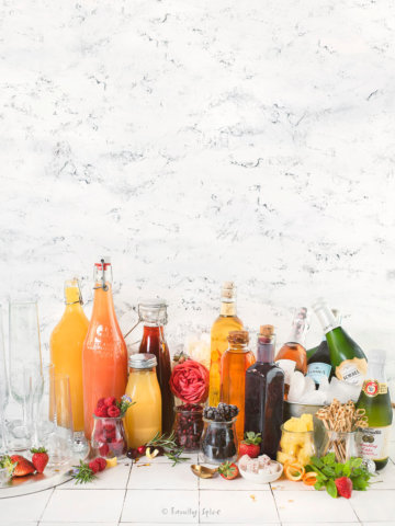 A champagne bar filled with many glass bottles with assorted juices, fruit syrups, fruits and drinks