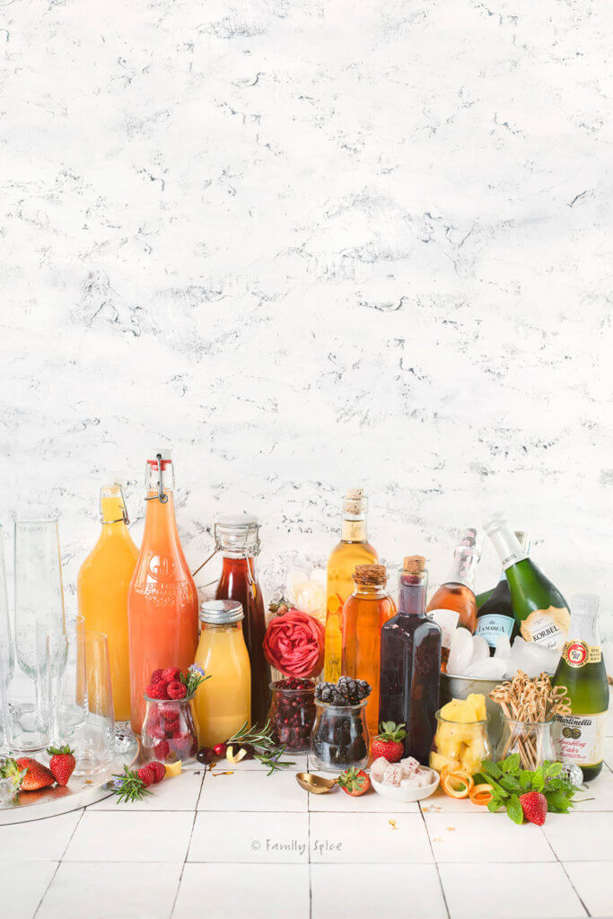 A champagne bar filled with many glass bottles with assorted juices, fruit syrups, fruits and drinks