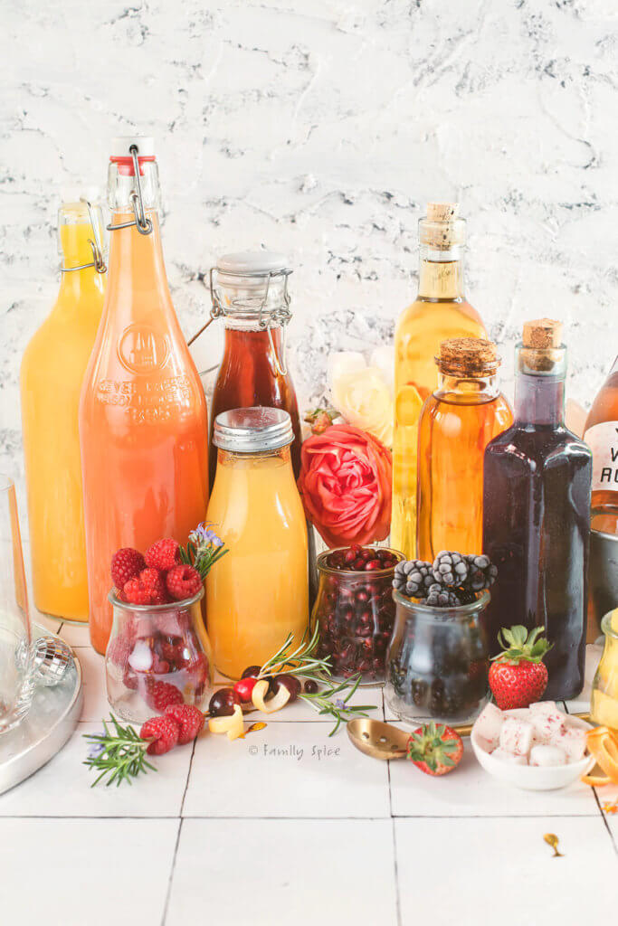 Assorted juice and fruit syrups in glass bottles with fruits around it
