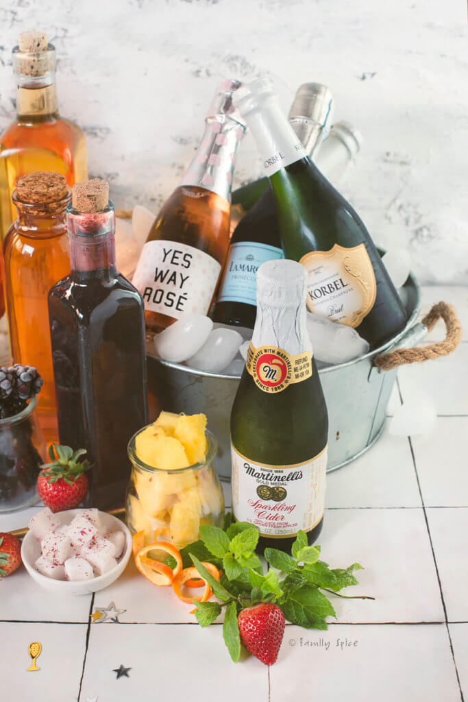A small metal bucket with assorted small bottles of sparkling wine with other fruit syrup bottles next to it