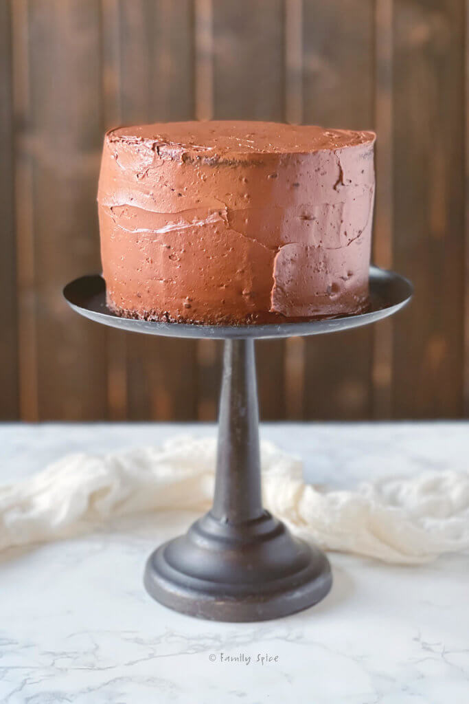 A 3 layer chocolate cake frosted in chocolate ganache frosting on a metal cake stand