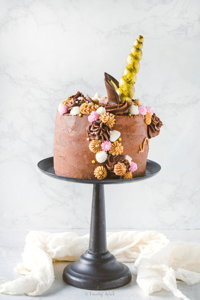 Side view of a chocolate unicorn cake on a metal cake stand