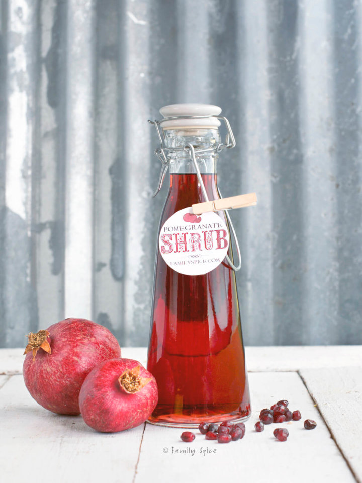 A bottle of pomegranate shrub with pomegranates next to it