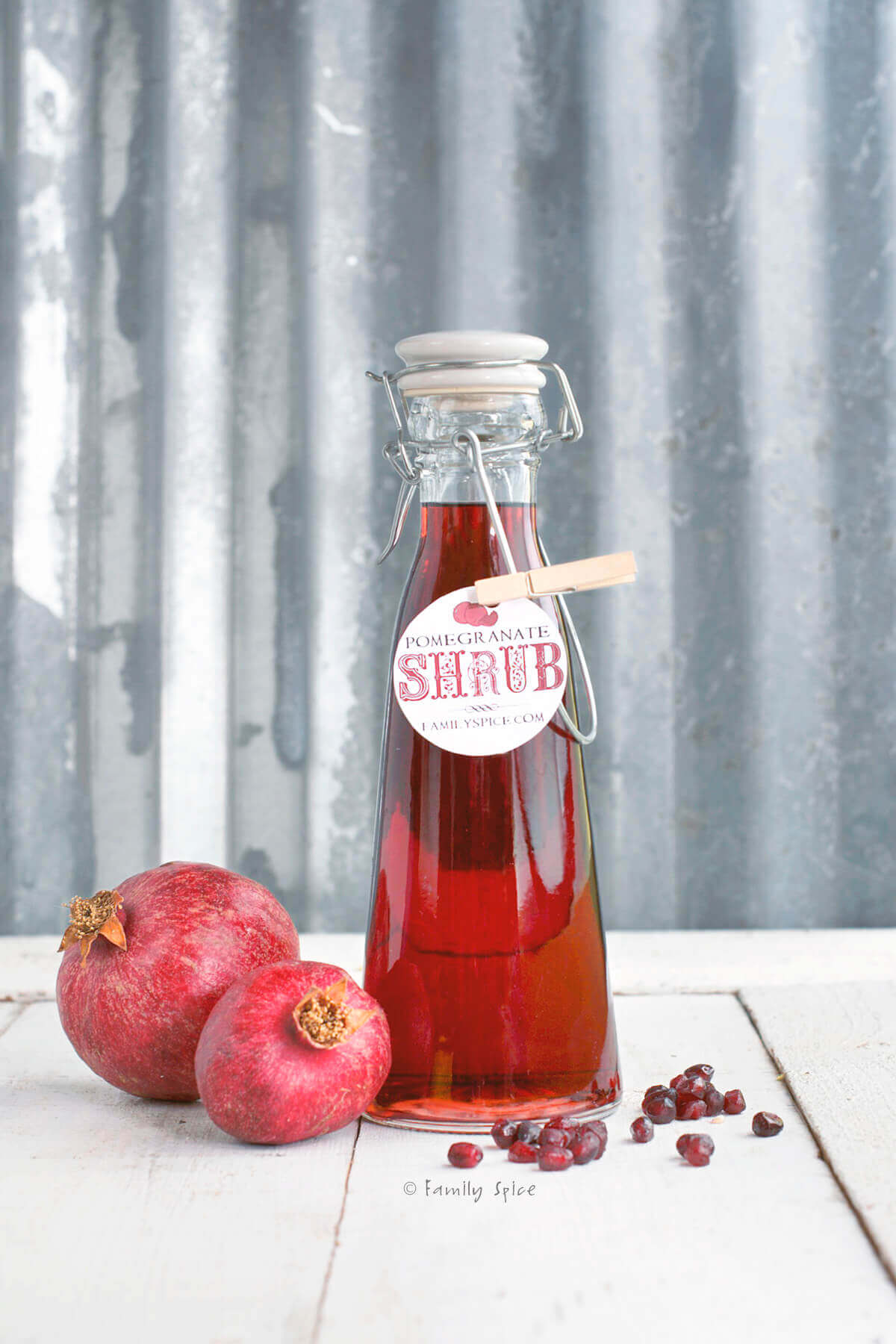 A bottle of pomegranate shrub with pomegranates next to it