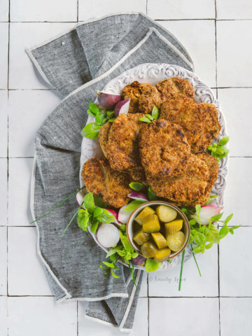 top view of a plate of ground turkey kotlet made in the air fryer on a white plate with herbs, pickles and radishes