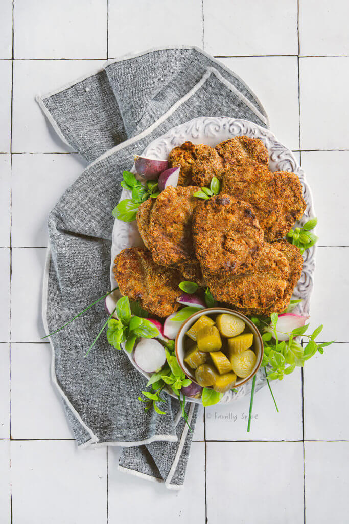 top view of a plate of ground turkey kotlet made in the air fryer on a white plate with herbs, pickles and radishes