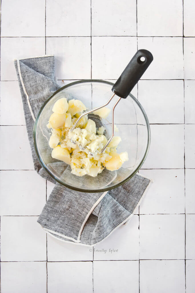 Cooked chunks of boiled potatoes in a glass bowl slightly mashed with a potato masher