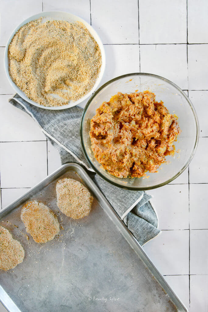 Ground turkey cutlet mixture in a glass mixing bowl with a small plate of bread crumbs with formed cutlet on a baking sheet