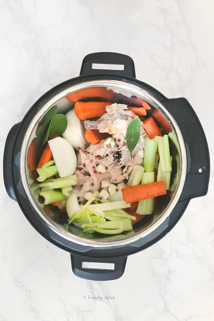 A chicken carcass with onions, celery, carrots, bay leaves and peppercorns inside an instant pot