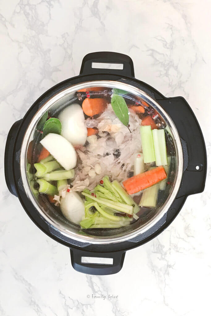 Covering chicken carcass and various vegetables with water in an instant pot to make bone broth