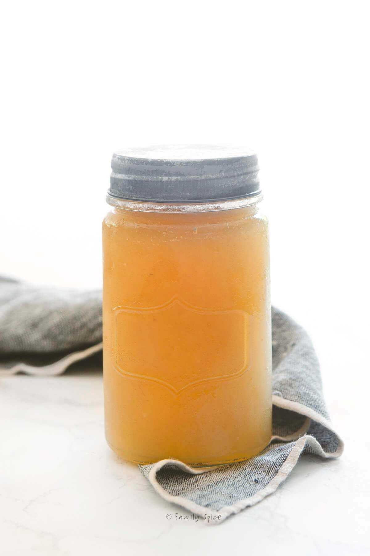 A mason jar filled with chicken bone broth with a napkin next to it