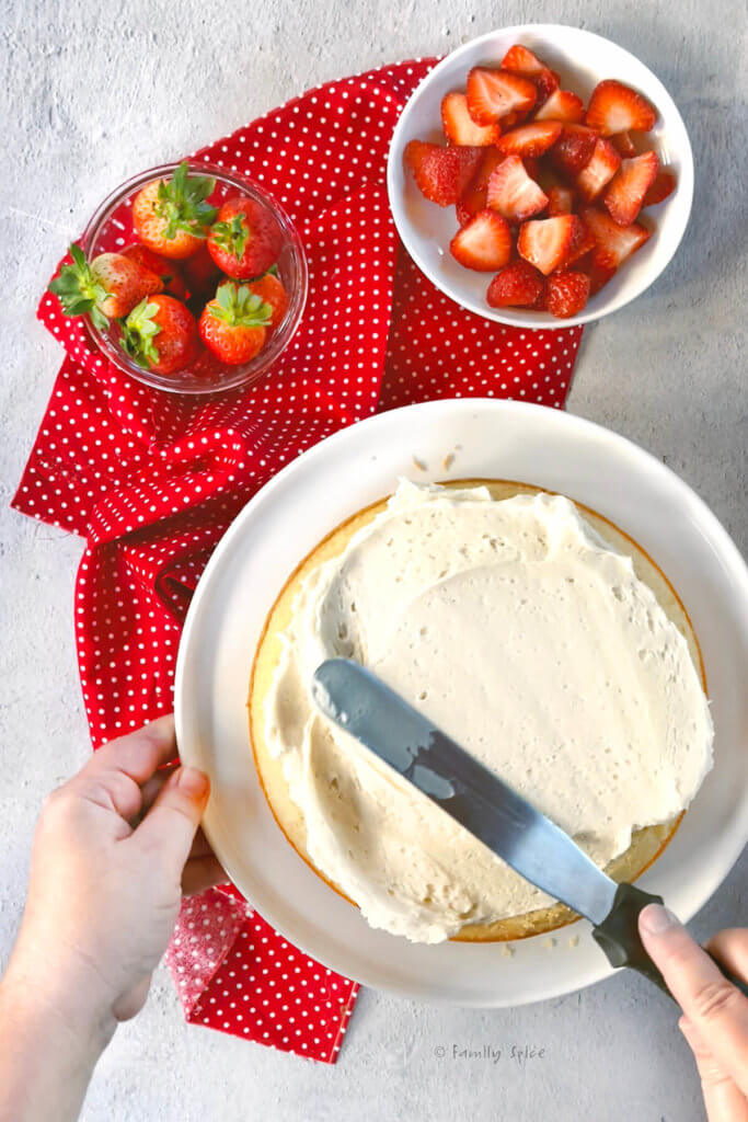 Frosting a vanilla olive oil cake with bowls of strawberries next to it