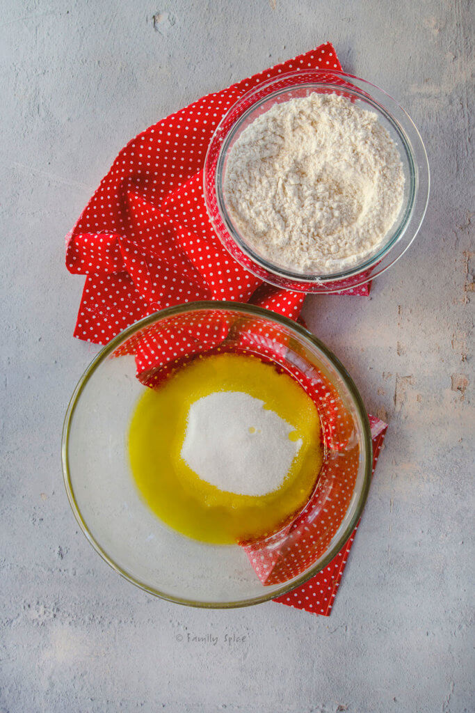 A large mixing bowl with olive oil and sugar in it and a bowl of flour mix next to it