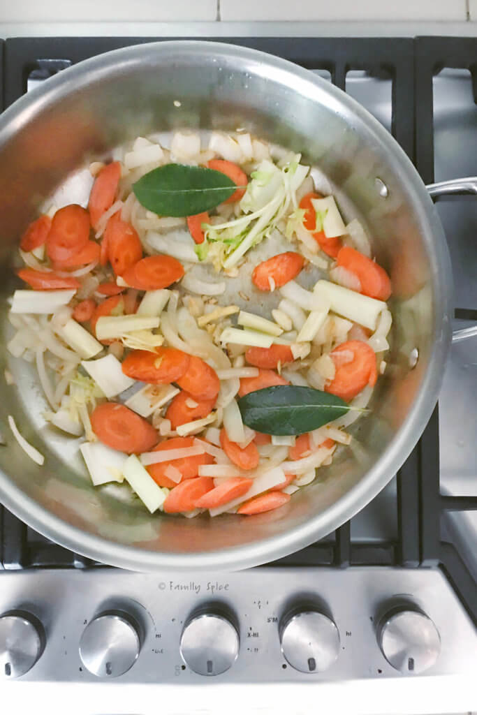 A large pot with onions, celery, carrots and bay leaves being sautéed