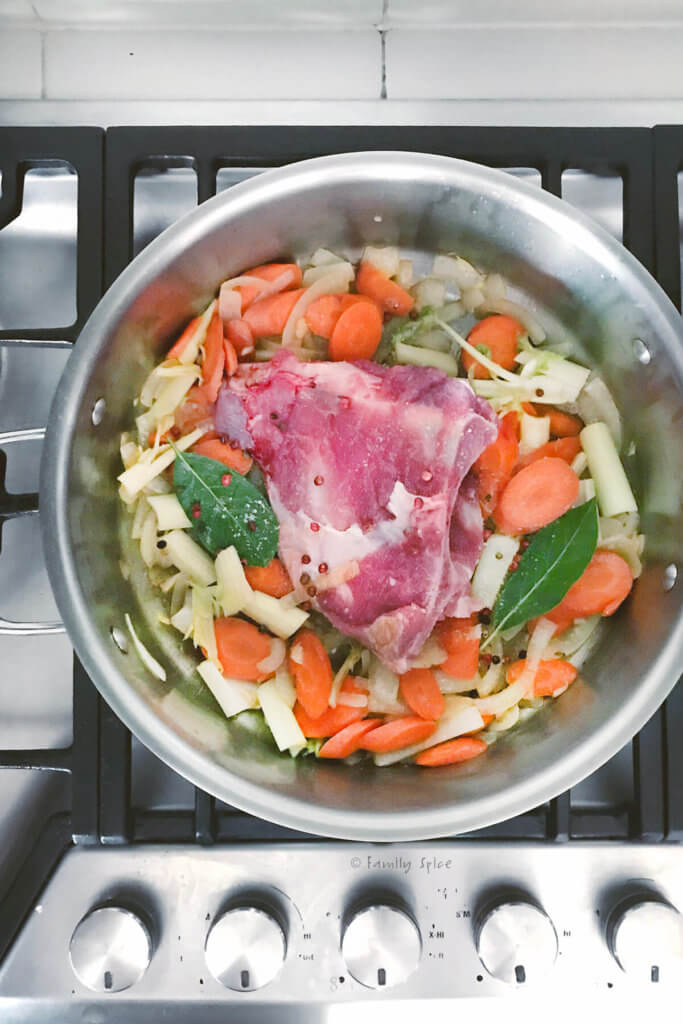 A large pot with a pork shoulder bone, onions, celery, carrots and bay leaves being sautéed