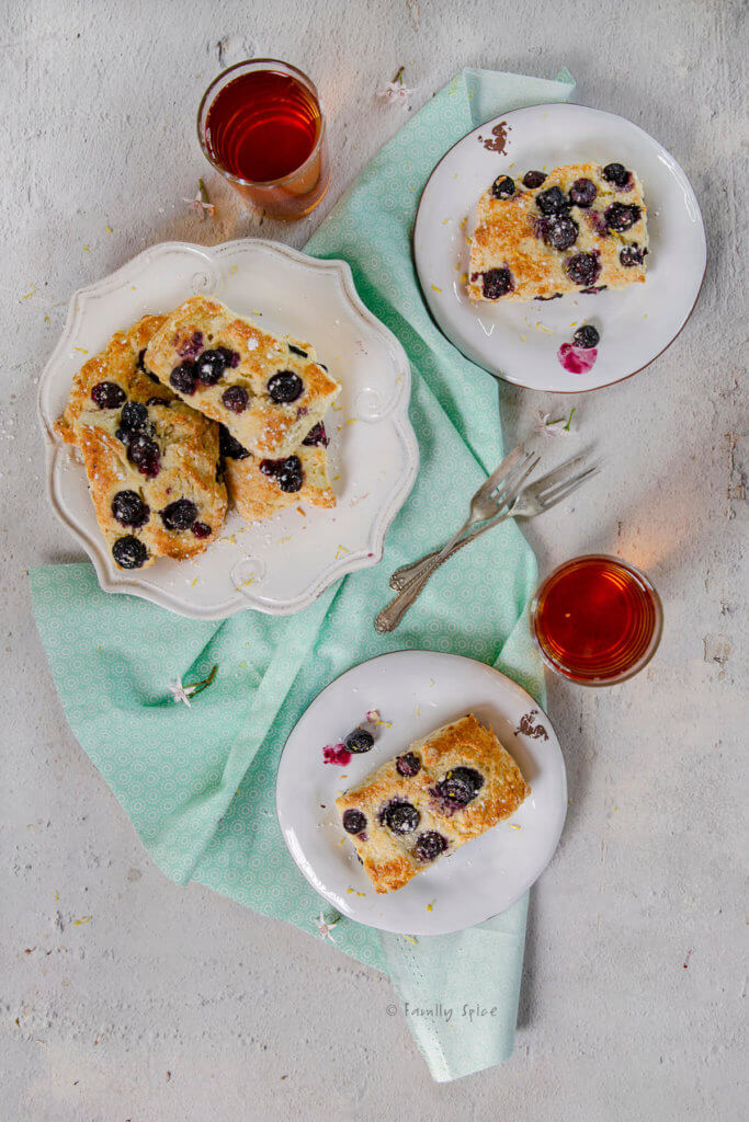 Top view of a plate full of blueberry scones with two smaller plates with scones on it with two glasses of tea next to it