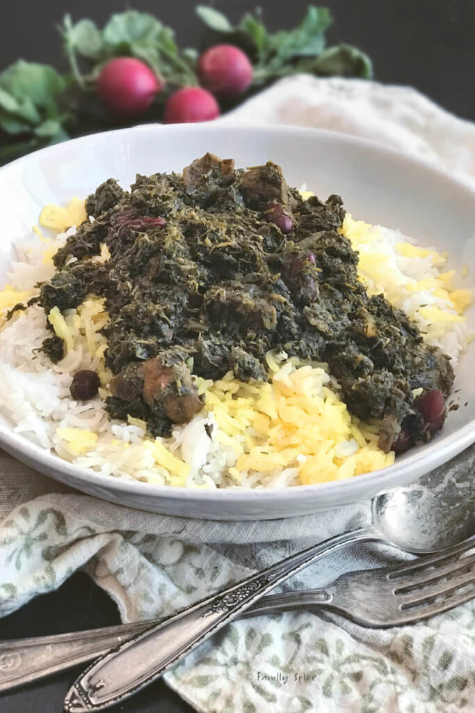Closeup of a plate with basmati rice topped with saffron and gormeh sabzi with radishes behind it