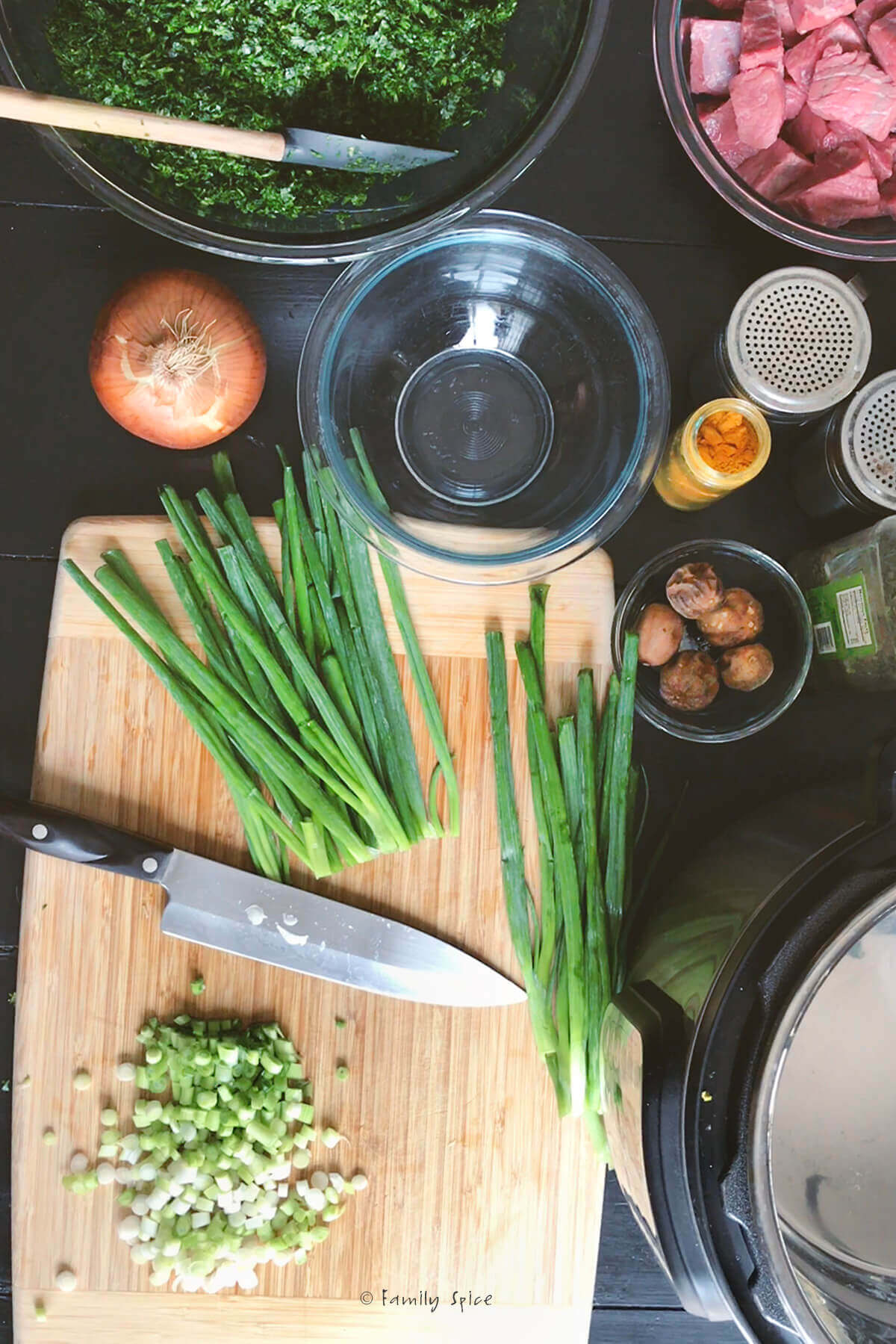 Chopping green onions on a wooden cutting board with other ingredients next to it