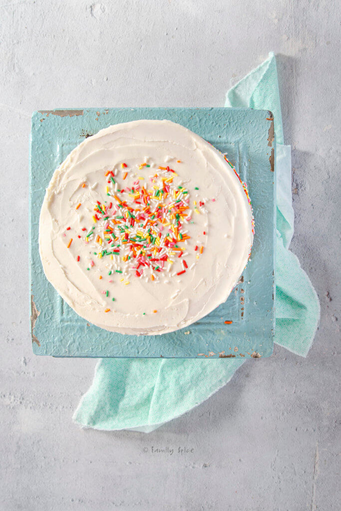 Top view of a vegan birthday cake covered with colorful sprinkles on a turquoise blue cake stand