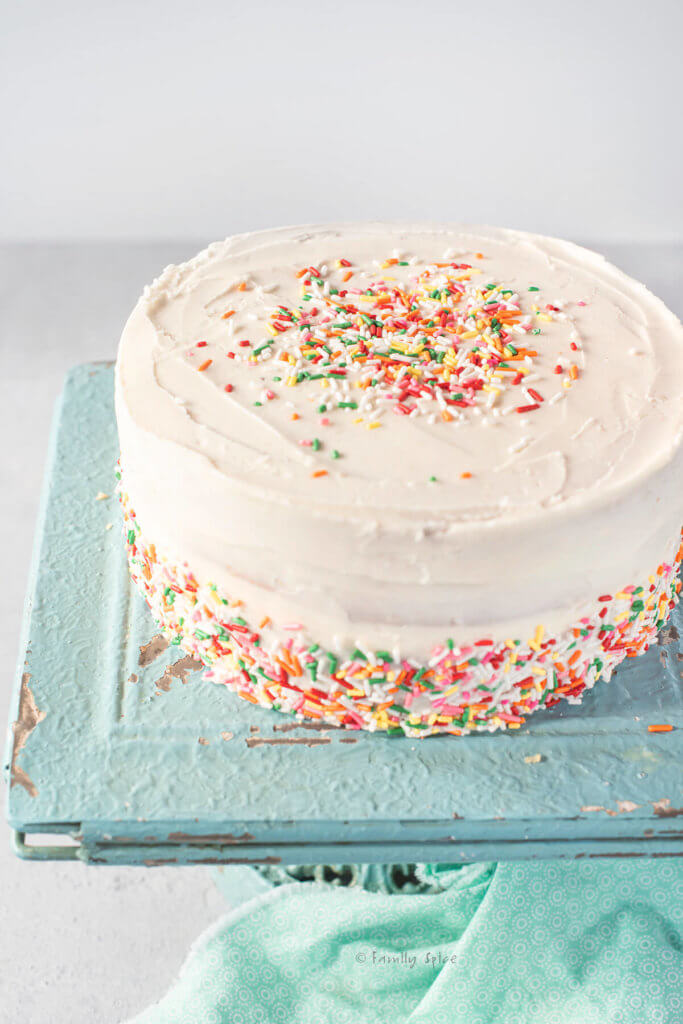 Closeup of a vegan birthday cake covered with colorful sprinkles on a turquoise blue cake stand