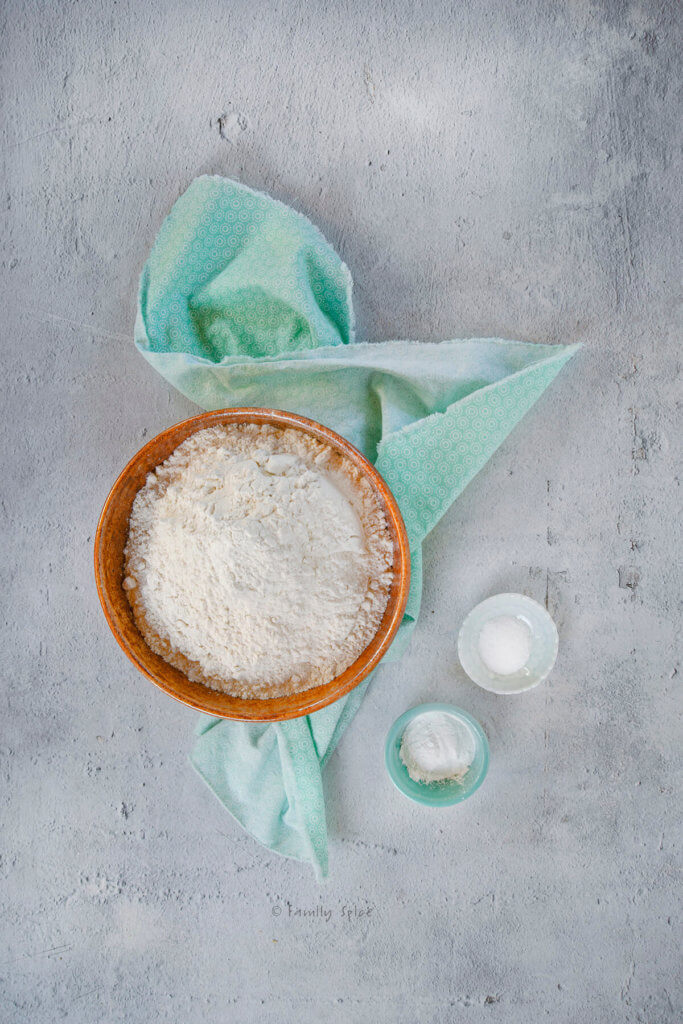 A bowl with flour with a small bowl of baking powder and another small bowl of salt next to it