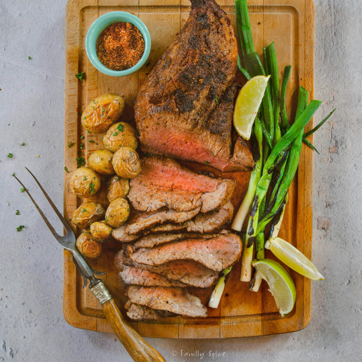 Top view of a roasted tri tip sliced up with potatoes and green onions on a cutting board