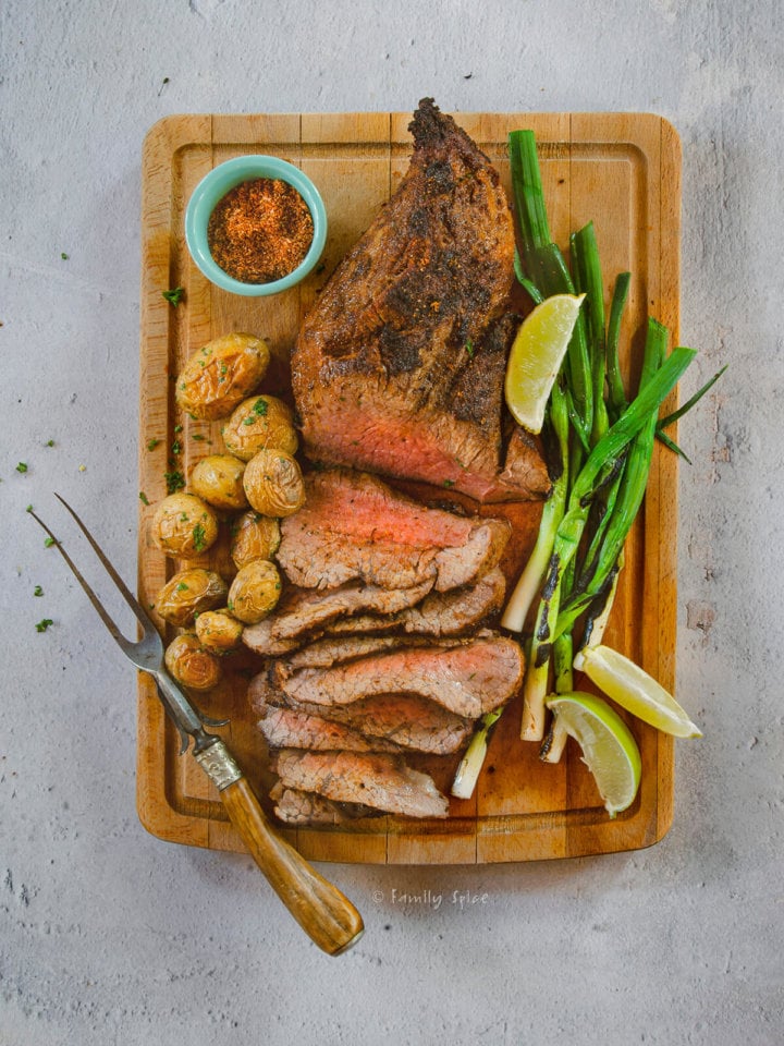 Top view of a roasted tri tip sliced up with potatoes and green onions on a cutting board