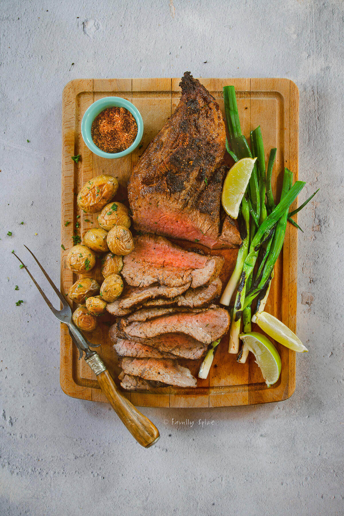 Top view of a roasted tri tip sliced up with potatoes and green onions on a cutting board