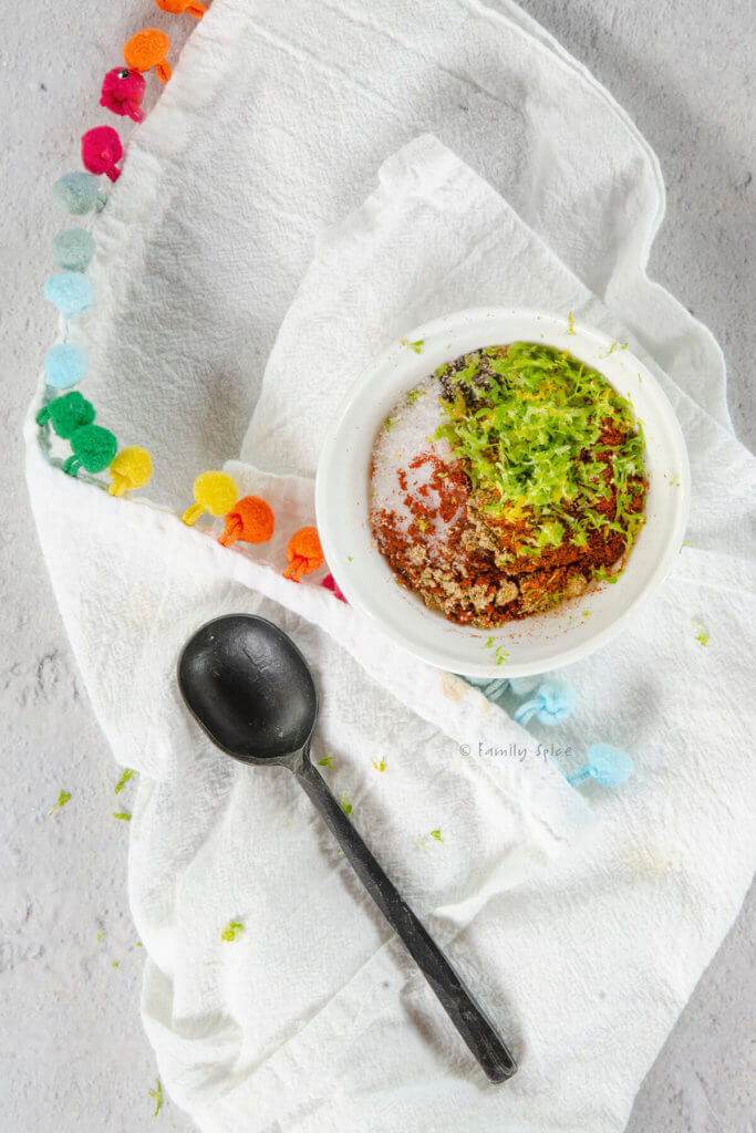 Chili lime seasoning in a small white bowl on a white kitchen towel with spoon next to it