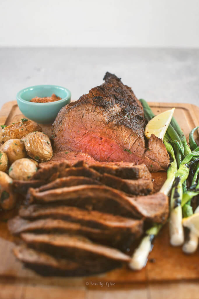 Closeup of a roasted tri tip carved with potatoes and green onions on a cutting board