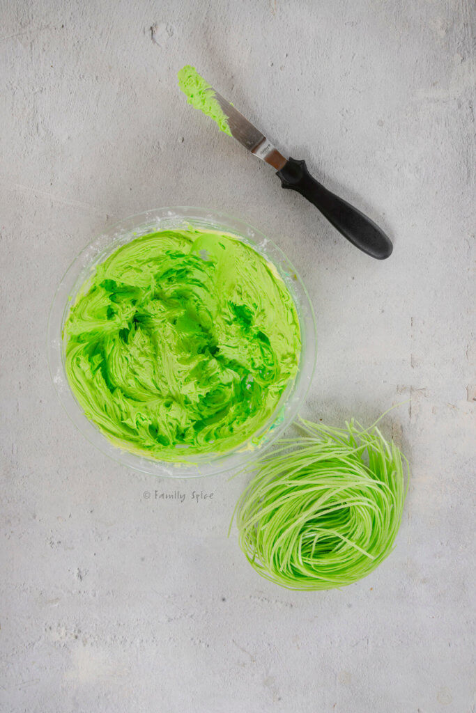 A bowl with bright green frosting, a palette knife and edible grass