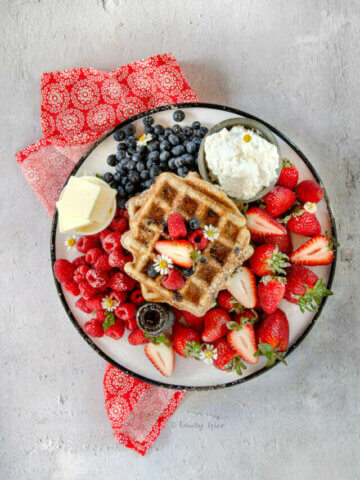 Top view of a round enamel platter with chocolate chip waffles, fresh berries, syrup, whipped cream and butter