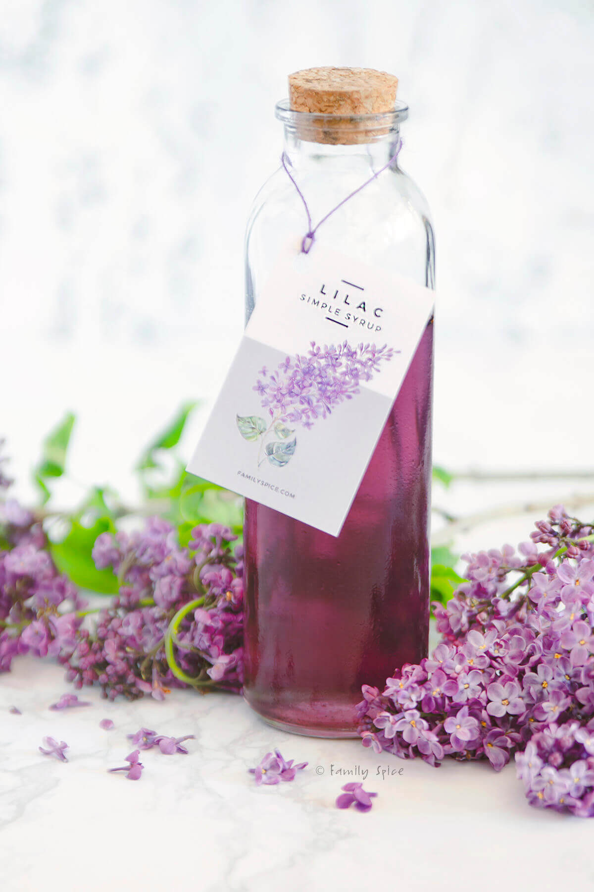 A bottle of lilac syrup with a homemade label on it and fresh lilacs around it