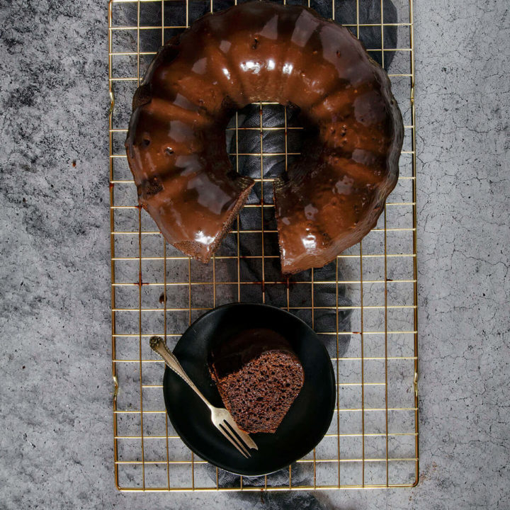 Chocolate guinness bundt cake with chocolate ganache with a slice cut out and on a dark plate next to it