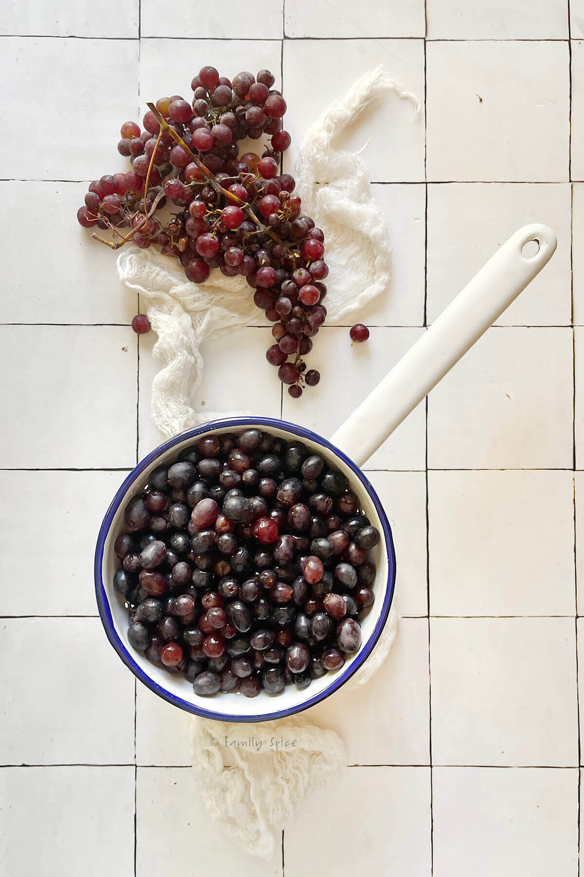 A white enamel strainer with stemmed red grapes in it and more red grapes next to it