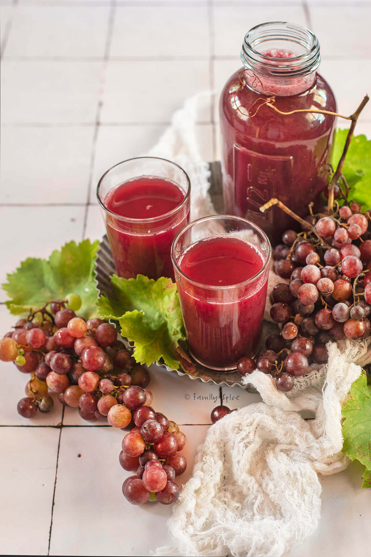 Closeup of a two glasses of homemade grape juice with a bottle of juice on a metal tray with fresh red grapes