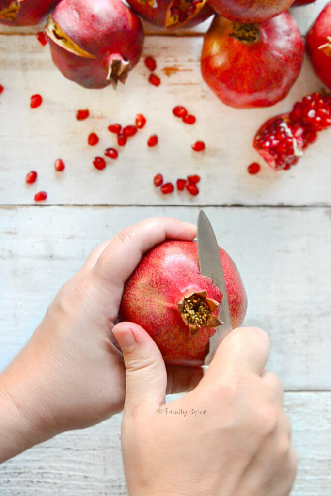 A hand cutting the crown from the top of a pomegranate