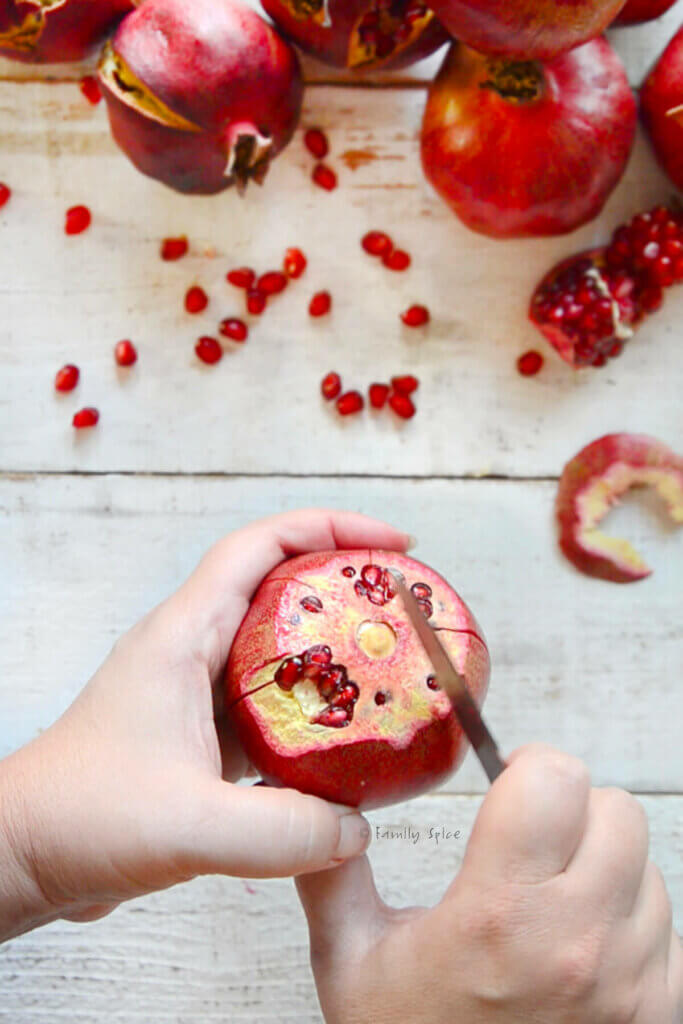 A hand holding a pomegranate with the crown remove and a knife scoring down the sides of the fruit