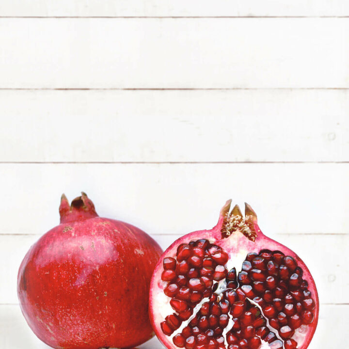 A whole pomegranate with a half pomegranate on a white background
