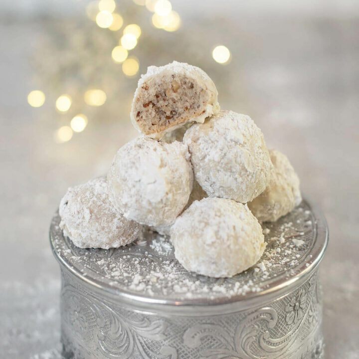 A mound of sand tarts with one on top halved on a silver pedestal with fairy lights behind it