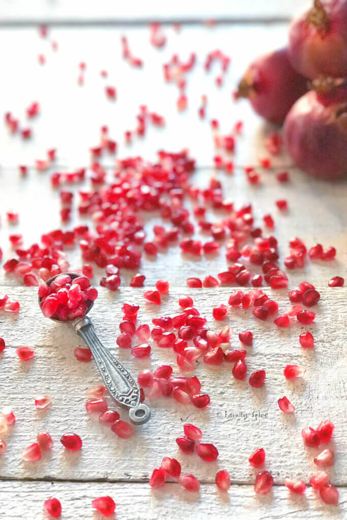 Side view of pomegranate arils scattered with a measuring spoon full of them