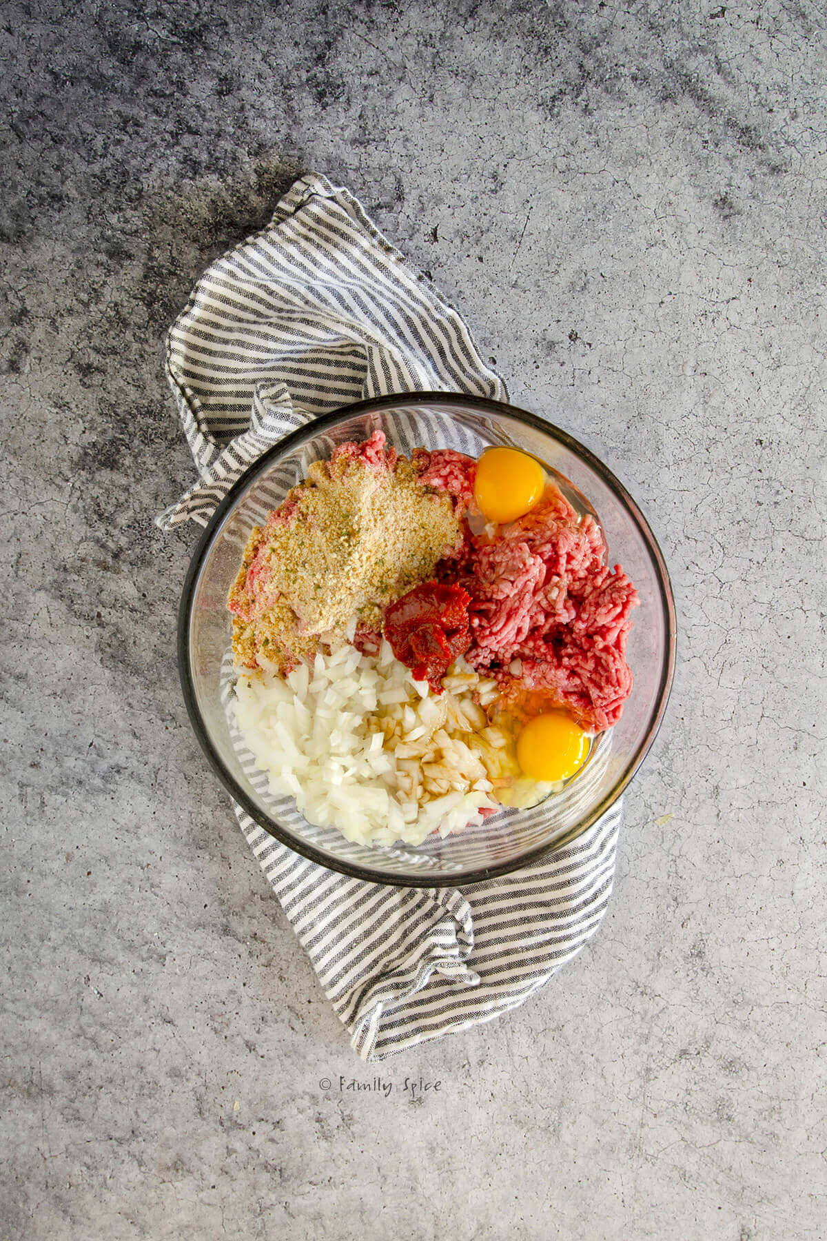 A glass mixing bowl with ingredients added to make meatloaf