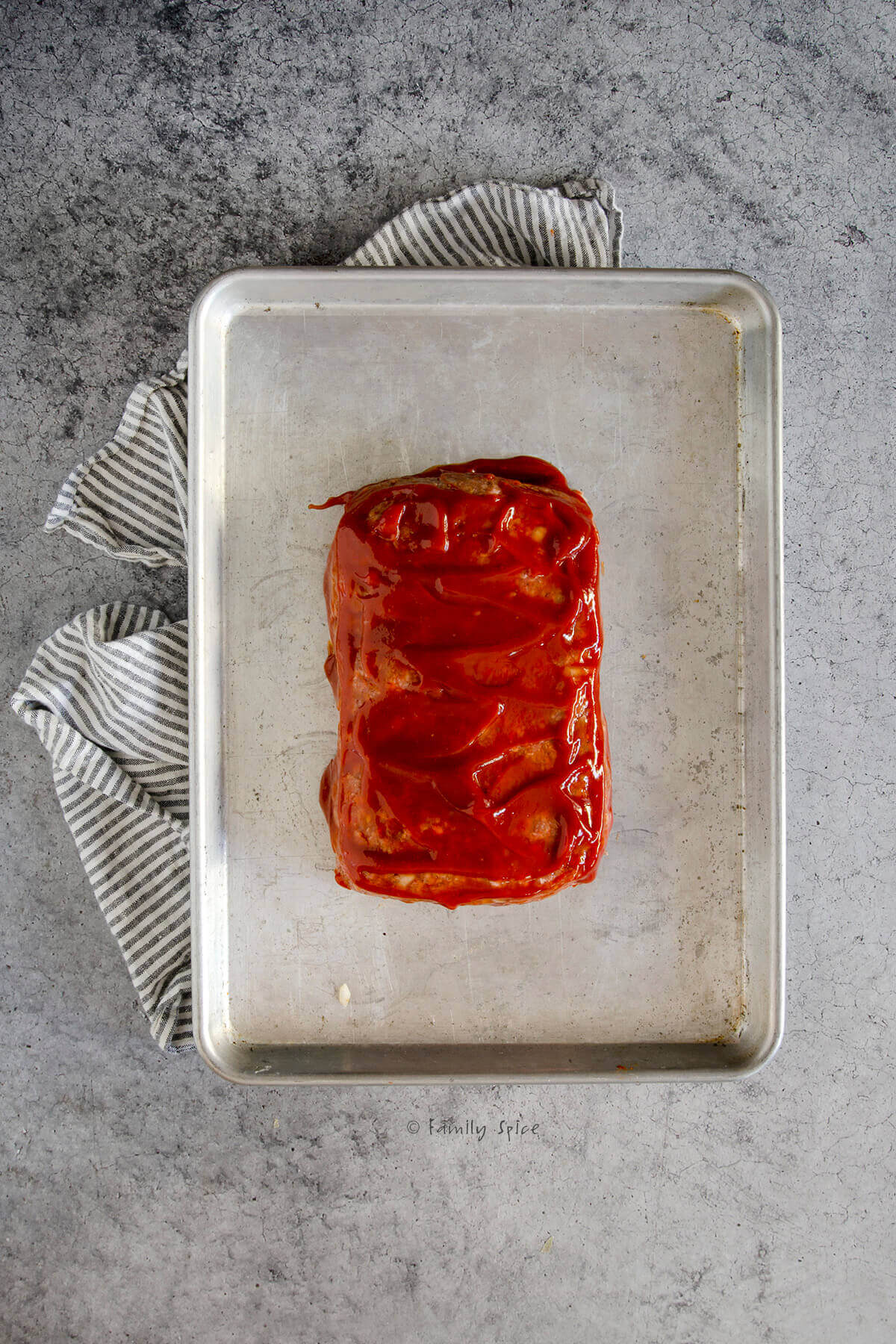 Meatloaf mixture formed into a rectangle topped with ketchup on a baking sheet
