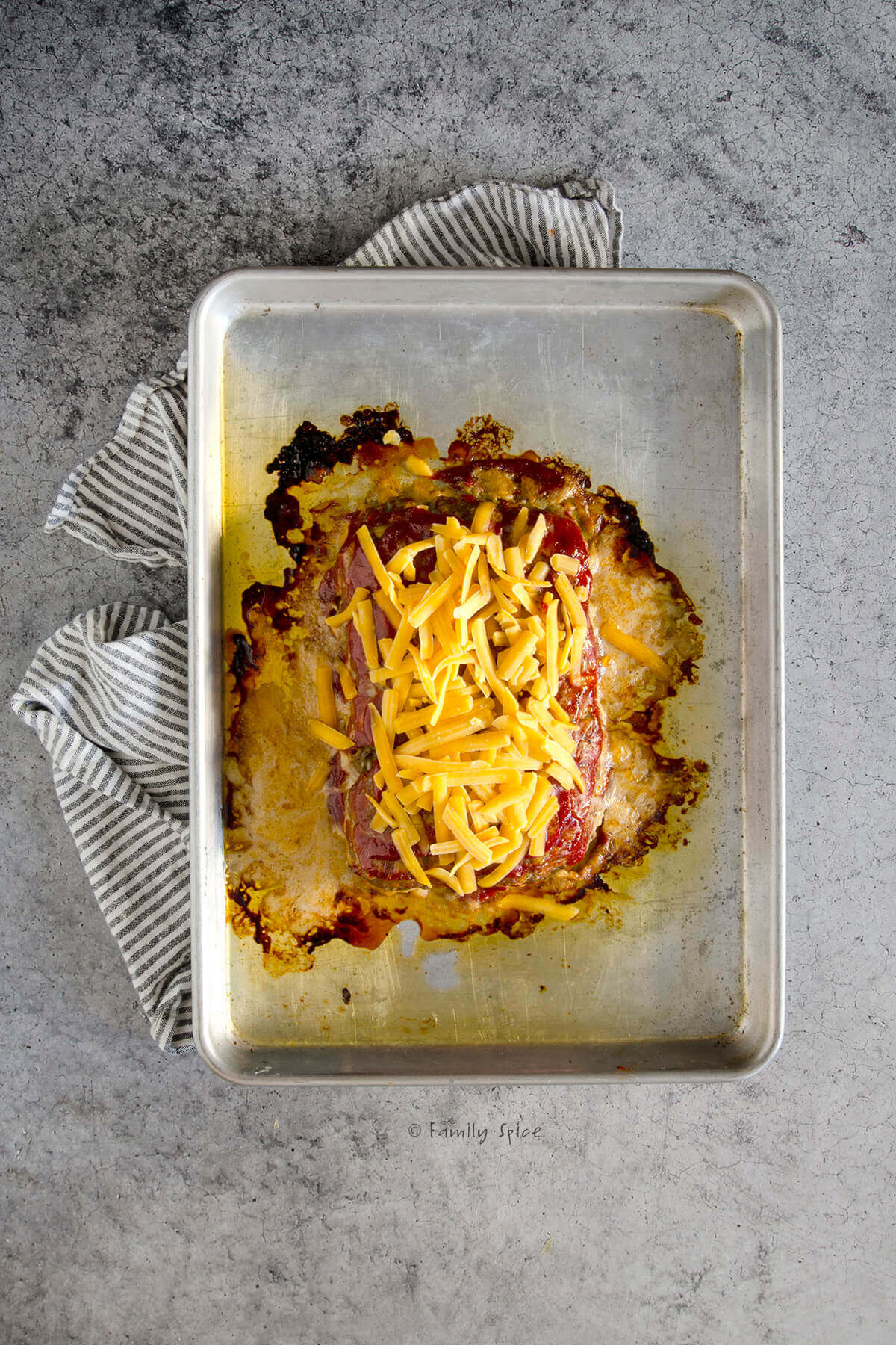 Shredded cheese topped on a freshly baked meatloaf on a baking sheet